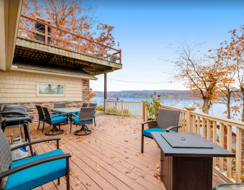 A scenic deck with blue chairs and a table, overlooking a lake surrounded by autumn foliage.