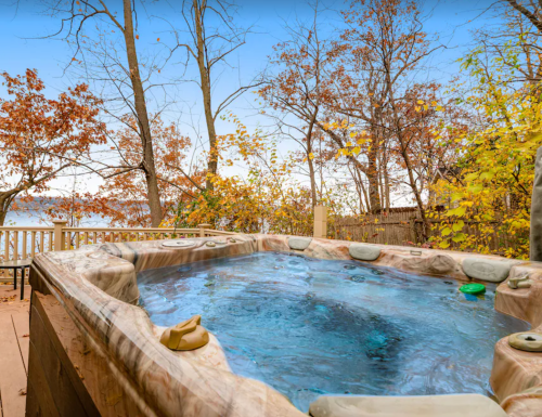 A hot tub surrounded by autumn trees and a lake in the background, showcasing vibrant fall foliage.