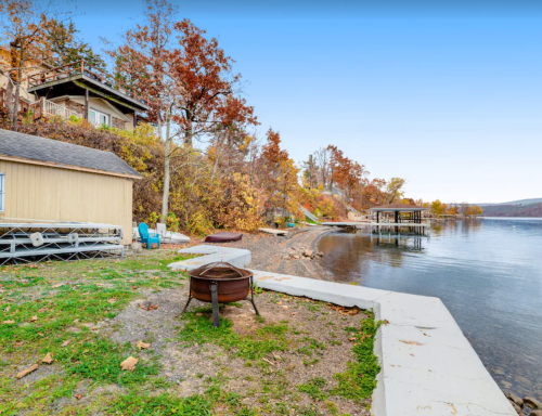 A serene lakeside view with autumn foliage, a dock, and a cozy cabin by the water's edge.