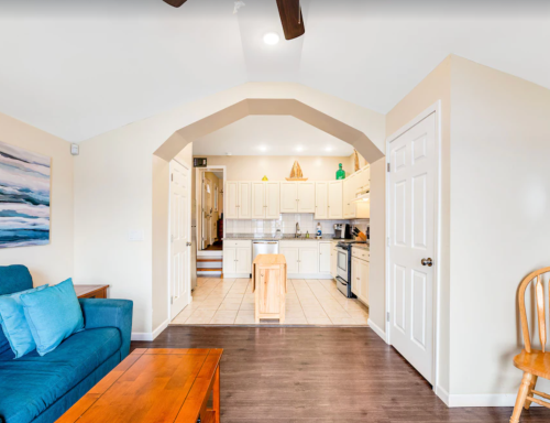 Cozy living area with blue couch, wooden table, and open kitchen in a well-lit, inviting space.