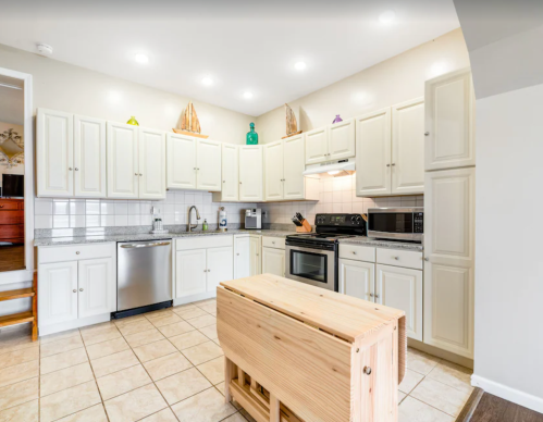 Bright kitchen with white cabinets, stainless steel appliances, and a wooden island in the center.
