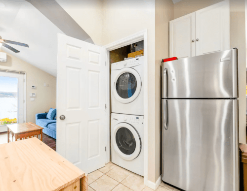 A laundry area with stacked washer and dryer next to a stainless steel refrigerator in a light-colored room.