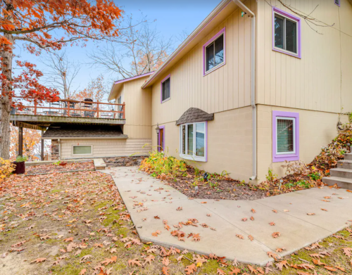 A modern house with purple accents, surrounded by autumn foliage and a patio area.