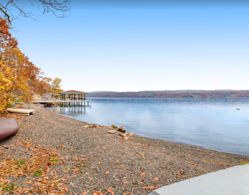 A serene lakeside view with autumn foliage, a dock, and calm water under a clear sky.