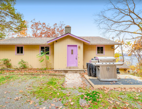 A cozy yellow house with a purple door, surrounded by autumn leaves and a grill on the patio.