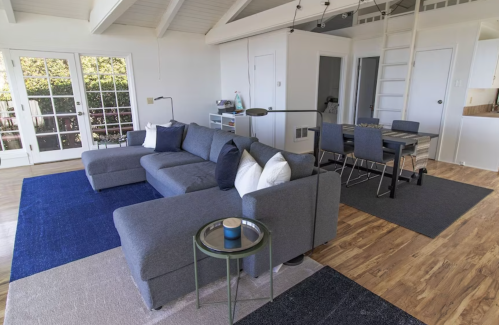 Modern living room with a gray sectional sofa, blue and beige rugs, and a dining area in a bright, open space.