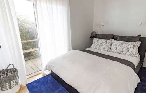 Cozy bedroom with a double bed, white bedding, and a sliding glass door leading to a wooden deck.