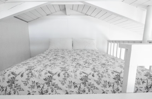 Cozy loft bedroom with a white bedspread and two pillows under a sloped ceiling.