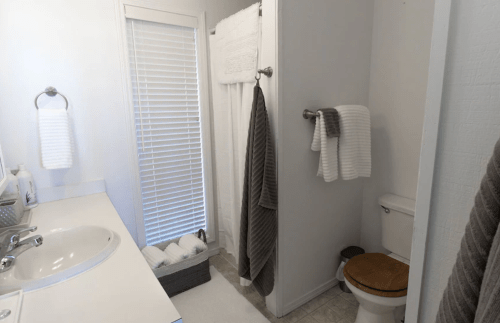 A clean, modern bathroom featuring a sink, shower, toilet, and neatly arranged towels in neutral colors.