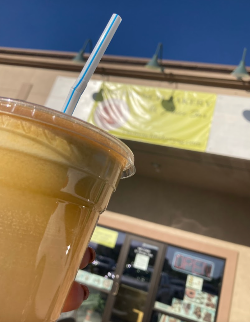 A hand holding a large iced drink in front of a store with a bright yellow sign and clear blue sky.