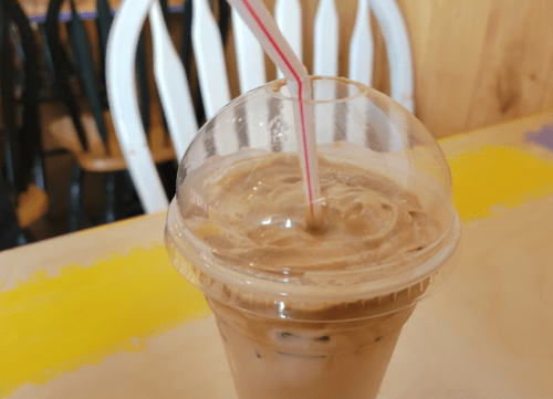 A clear cup of iced coffee with a straw, sitting on a colorful table in a café.