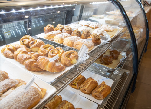 A display case filled with various pastries, including croissants and sweet rolls, neatly arranged on trays.