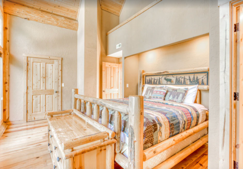 Cozy bedroom with a wooden bed, colorful quilt, and rustic decor, featuring warm lighting and wooden walls.
