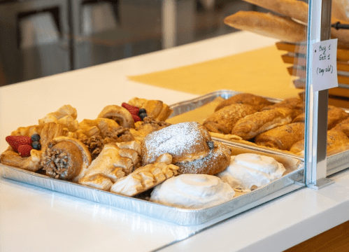 A tray of assorted pastries, including croissants, danishes, and cinnamon rolls, displayed in a bakery setting.