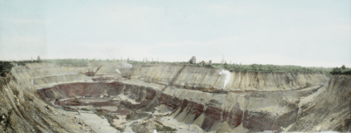 A panoramic view of a large mining site with steep, layered earth and machinery in the background.