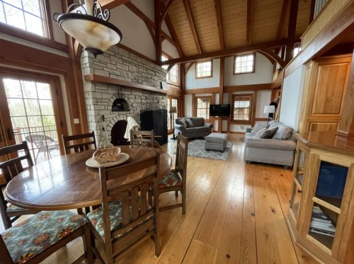 Cozy cabin interior with wooden beams, stone fireplace, dining table, and comfortable seating area.