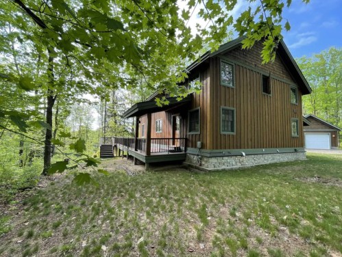 A wooden house surrounded by trees, featuring a porch and a grassy yard.