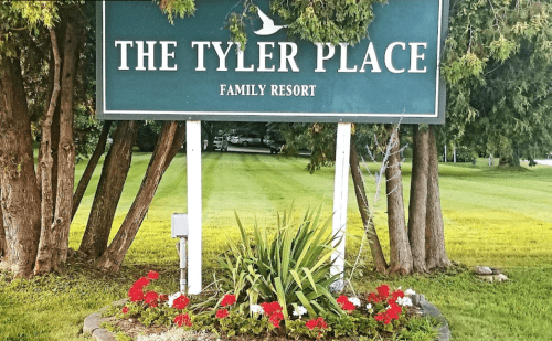 Sign for "The Tyler Place Family Resort" surrounded by greenery and colorful flowers.