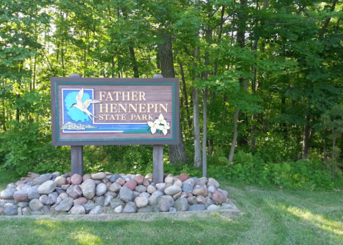 Sign for Father Hennepin State Park, surrounded by greenery and rocks, indicating the park's entrance.