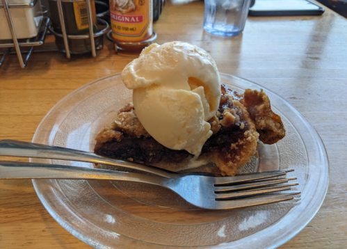 A slice of chocolate pie topped with a scoop of vanilla ice cream on a clear plate, with forks beside it.
