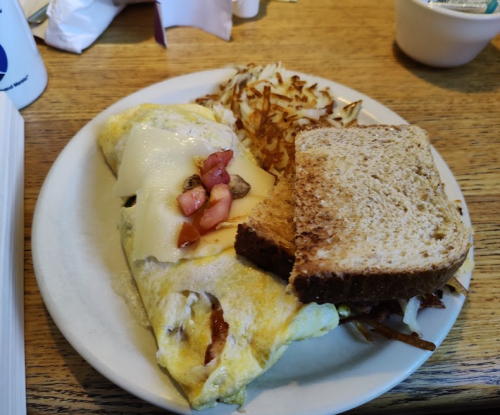 A plate with an omelette topped with cheese and tomatoes, hash browns, and two slices of whole grain bread.