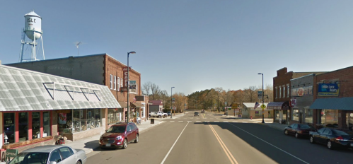 A small town street with shops on either side and a water tower in the background under a clear blue sky.