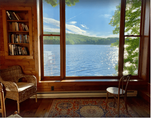 Cozy interior with a chair and bookshelf, featuring a scenic view of a sparkling lake and trees outside.