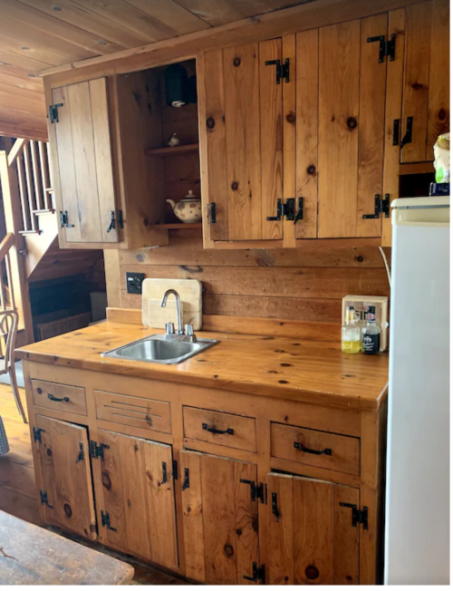A rustic wooden kitchen with cabinets, a sink, and a countertop, featuring a cozy, cabin-like atmosphere.