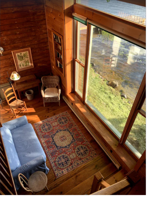 Cozy wooden interior with a blue sofa, rug, and large windows overlooking a serene outdoor view.