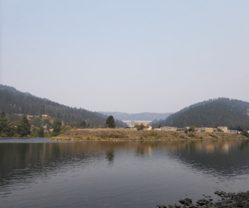 A serene lake surrounded by mountains, with a hazy sky and a small island in the foreground.