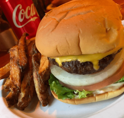 A cheeseburger with lettuce, tomato, and onion, served with crispy fries and a Coca-Cola in the background.