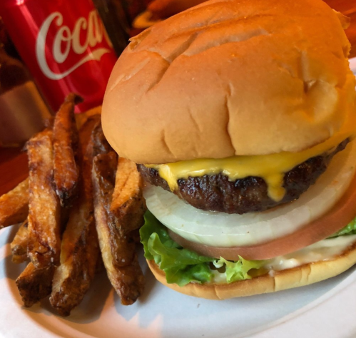 A cheeseburger with lettuce, tomato, and onion, served with crispy fries and a Coca-Cola in the background.