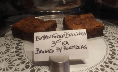 Two Butterfinger brownies displayed on a lace doily, with a sign stating "Banned by Bloomberg" and a price of $3.25 each.