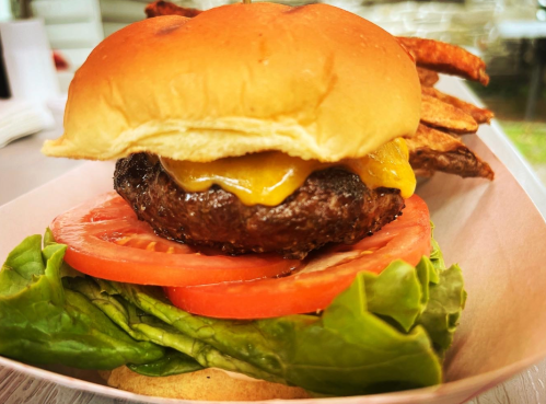 A close-up of a cheeseburger with lettuce, tomato, and a toasted bun, served with crispy potato wedges.