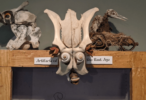A display of unique artifacts labeled "Artifacts of the Rust Age," featuring a decorative mask and animal sculptures.