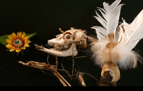 A whimsical sculpture featuring a skull with feathers and a flower, all adorned with colorful eyes.