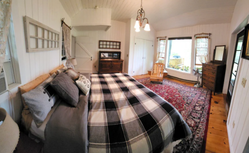 Cozy bedroom with a large bed, patterned rug, wooden furniture, and natural light from windows.
