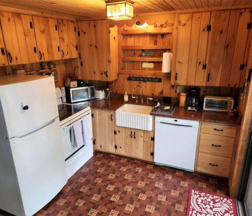Cozy wooden kitchen with appliances, a farmhouse sink, and a patterned floor. Warm, inviting atmosphere.