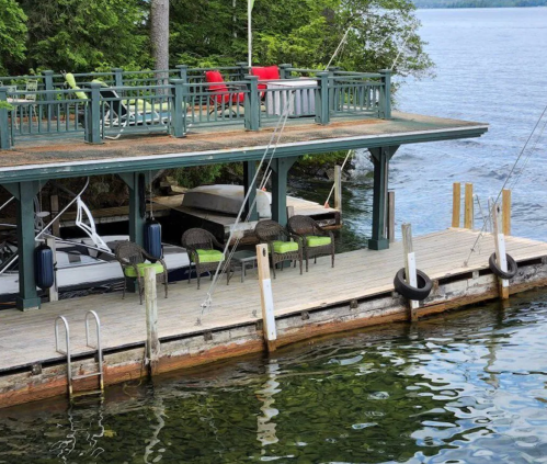 A lakeside dock with chairs and a deck overlooking calm water, surrounded by trees.
