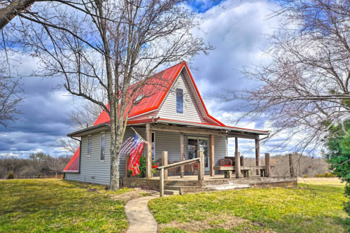 A charming house with a red roof, surrounded by trees and a grassy yard, under a cloudy sky.