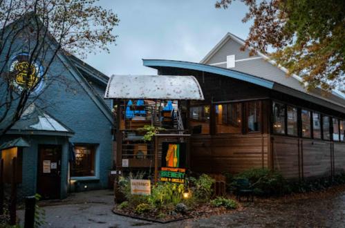 A brewery with a modern wooden exterior and large windows, surrounded by trees on a cloudy day.