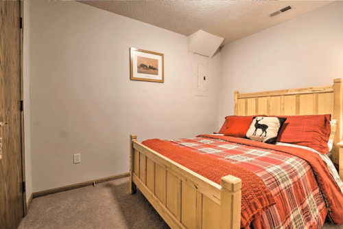 Cozy bedroom featuring a wooden bed with red and plaid bedding, a framed picture on the wall, and neutral-colored walls.