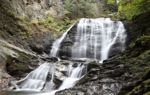 A serene waterfall cascading over rocky terrain, surrounded by lush greenery and rugged cliffs.