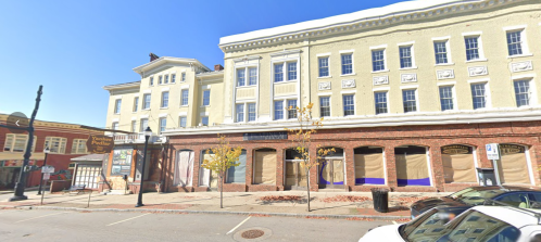 Historic building with yellow facade and brick base, featuring boarded windows and a clear blue sky above.