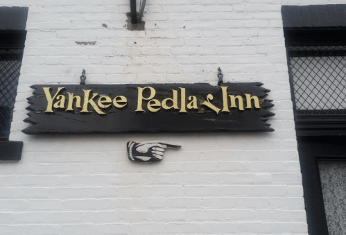 Sign for "Yankee Pedlar Inn" with a pointing hand, mounted on a white brick wall.