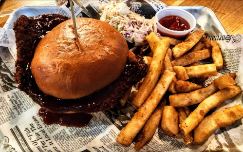 A crispy fried chicken sandwich with sauce, served with coleslaw and golden fries on a tray lined with newspaper.