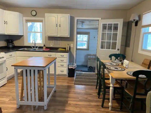 Cozy kitchen with white cabinets, a wooden table, and a door leading to a small entryway. Natural light fills the space.