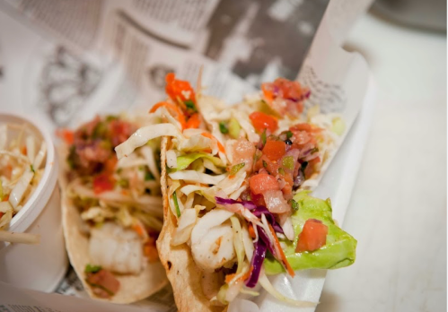 Three tacos filled with shrimp, fresh vegetables, and salsa, served in a paper-lined basket.