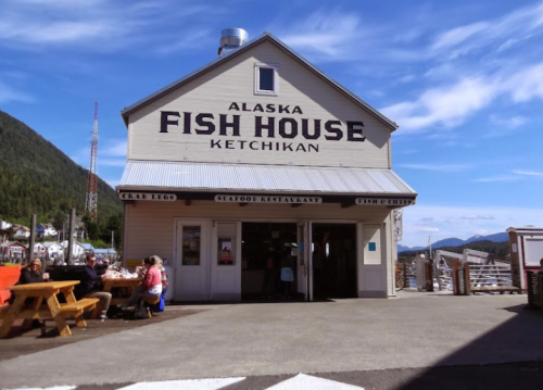 Exterior of Alaska Fish House in Ketchikan, featuring a sign and outdoor seating with mountains in the background.