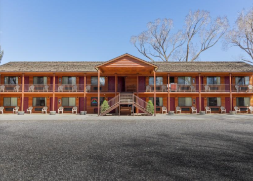 A two-story wooden lodge with balconies, surrounded by trees and a gravel parking area.